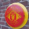 Handmade red and yellow circular sign featuring the Manchester United Football Club badge.